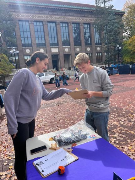 A Turn Up Turnout volunteer helping a student fill out a form on the Diag